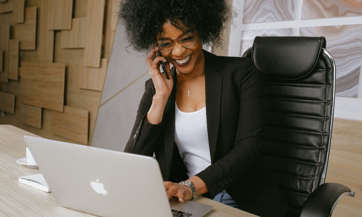 woman wearing black blazer sitting at a desk talking on cell phone