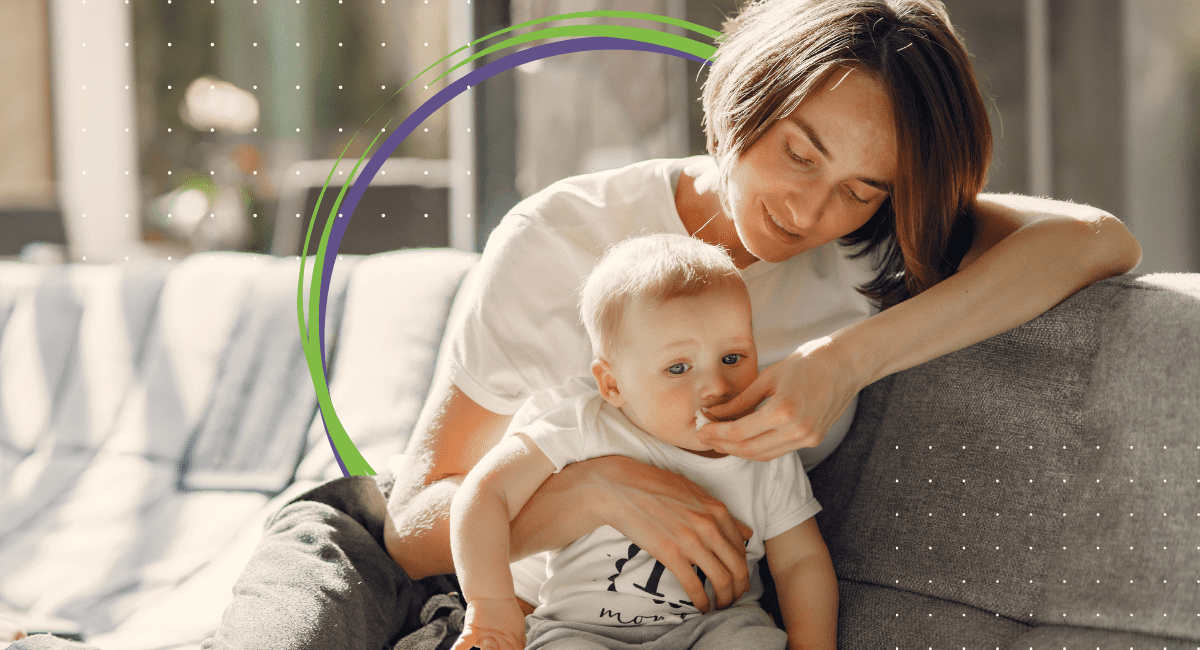 Mother and baby sitting on couch, mom wiping baby's mouth in sunny living room