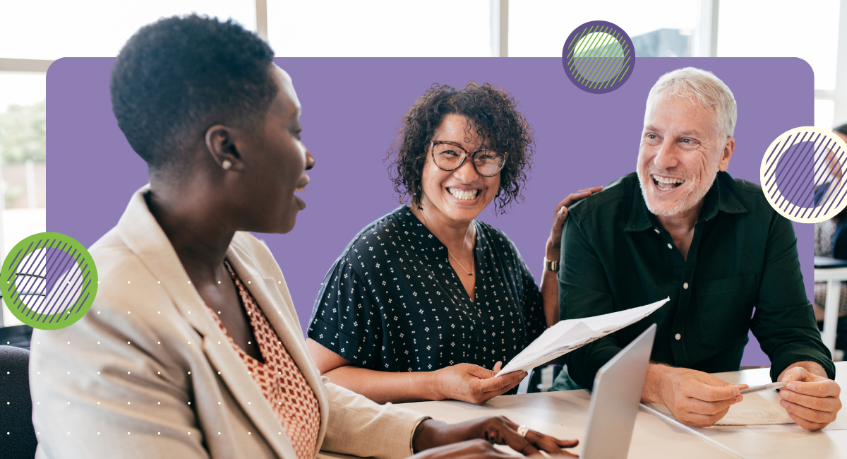 Three adults sitting at a table smiling while reviewing paperwork