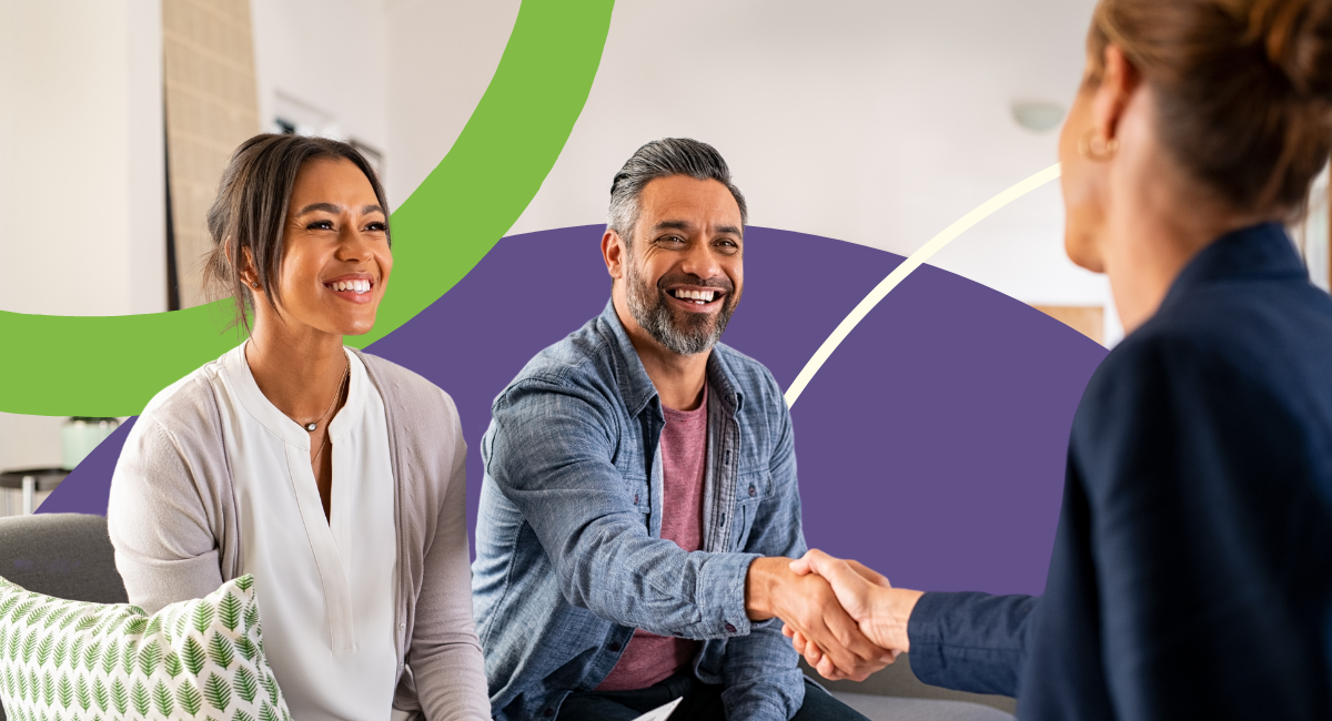 Man and woman sitting on a gray couch, man is shaking hands with a woman in an office.