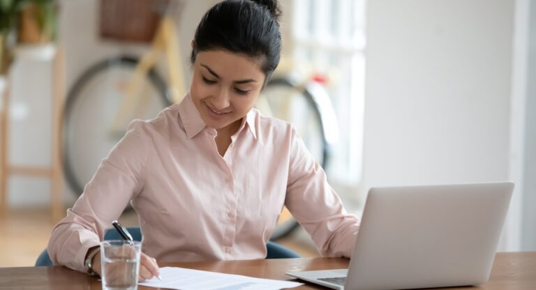 Young woman with dark hair filling out a form sitting at a desk