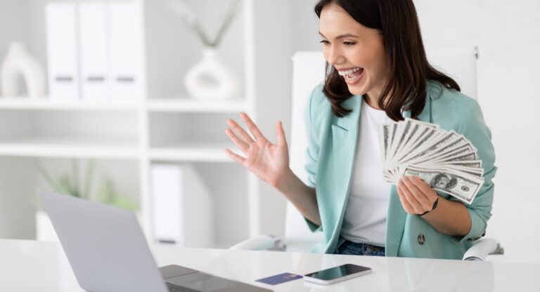 Happy young woman holding cash sitting in an office