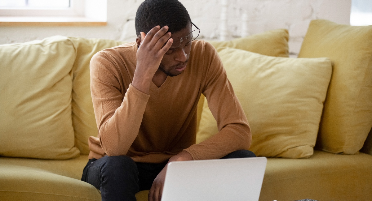 Upset man touching head using calculator and laptop