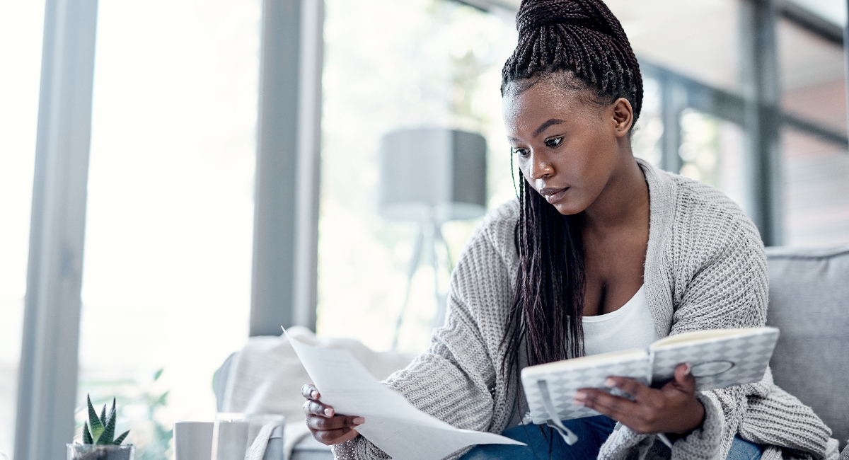 Woman reading student loan information, sitting on a couch and holding a piece of paper