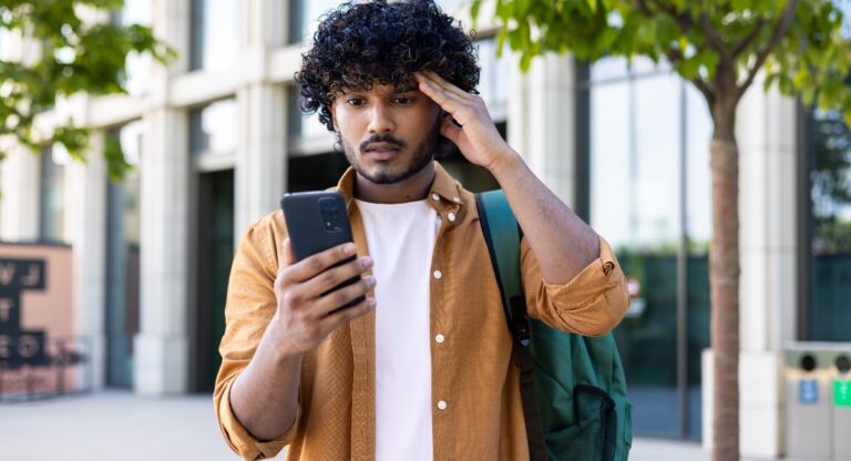Upset student with backpack reads bad news on phone