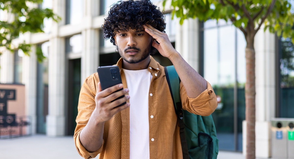 Upset student with backpack reads bad news on phone